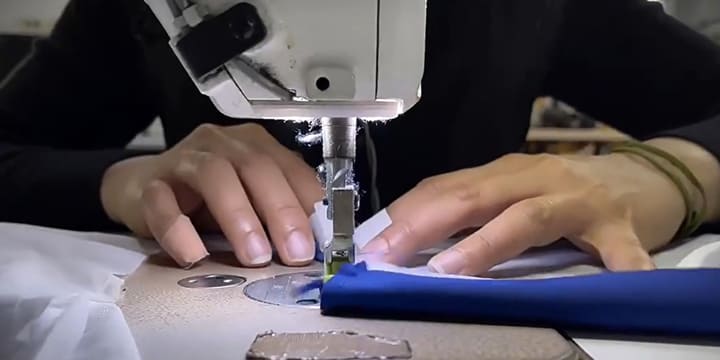 Close-up of hands operating a sewing machine, working on blue equestrian gear material, showcasing superior craftsmanship and attention to detail